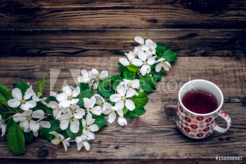 Picture of A branch of apple blossoms and a mug of tea on wooden background